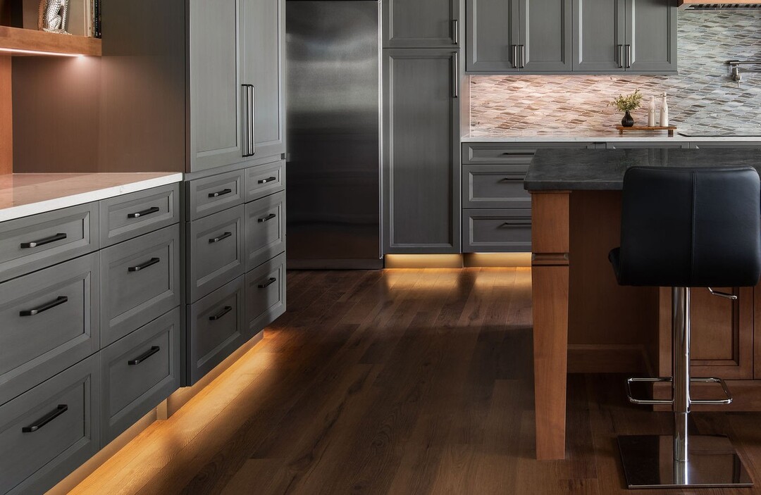 Modern kitchen with dark gray cabinets, hardwood floors, a wooden island, and integrated LED toe-kick lighting.