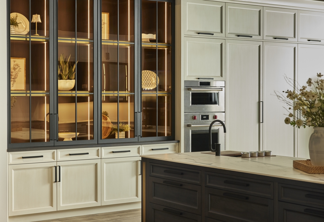 Elegant kitchen showcasing soft contrast with vintage glazed white cabinets, dark wood island, and illuminated glass displays.